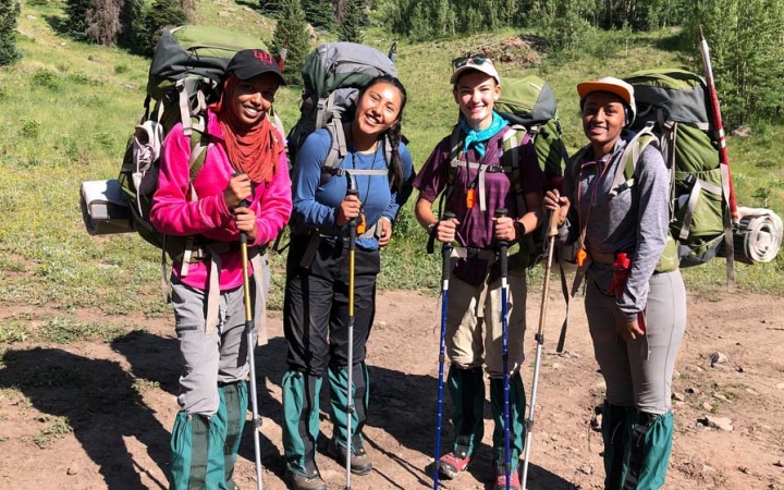 four outward bound students wearing backpacks smile at the camera